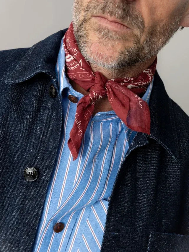 Man wearing the MOS MOSH Gallery Canada Martin paisley neckerchief in red, knotted at the neck over a blue striped shirt and dark denim jacket.