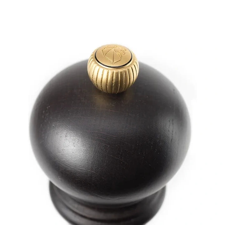 Black pepper grinder with a gold top on a white background