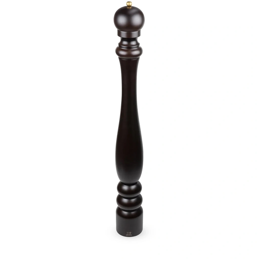 A tall, dark brown wooden pepper mill with a turned spindle design and a small brass top, shown on a plain white background.