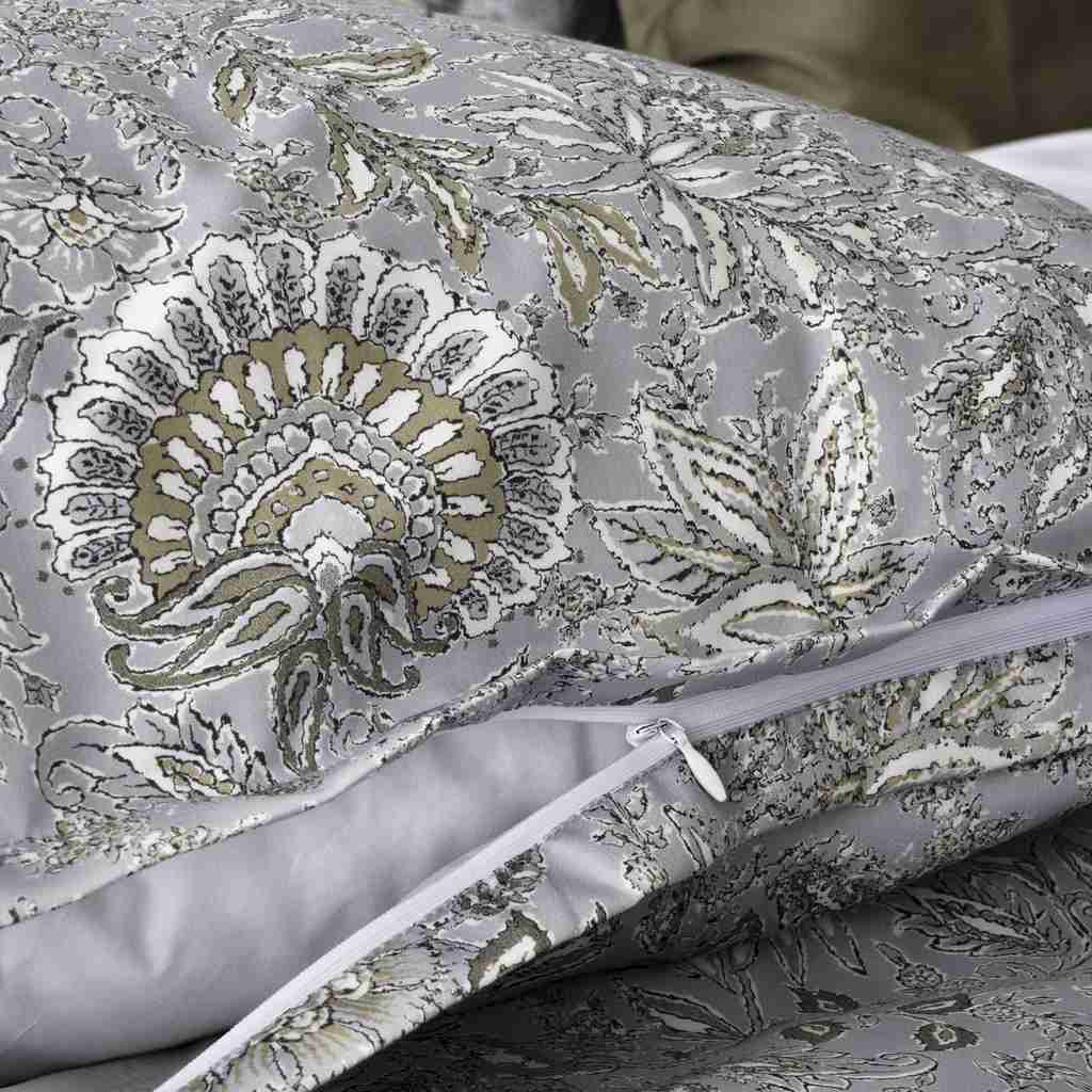 A close-up of a pillow sham with a woven floral and paisley pattern in gray, white, and muted gold, shown folded with a zipper visible.