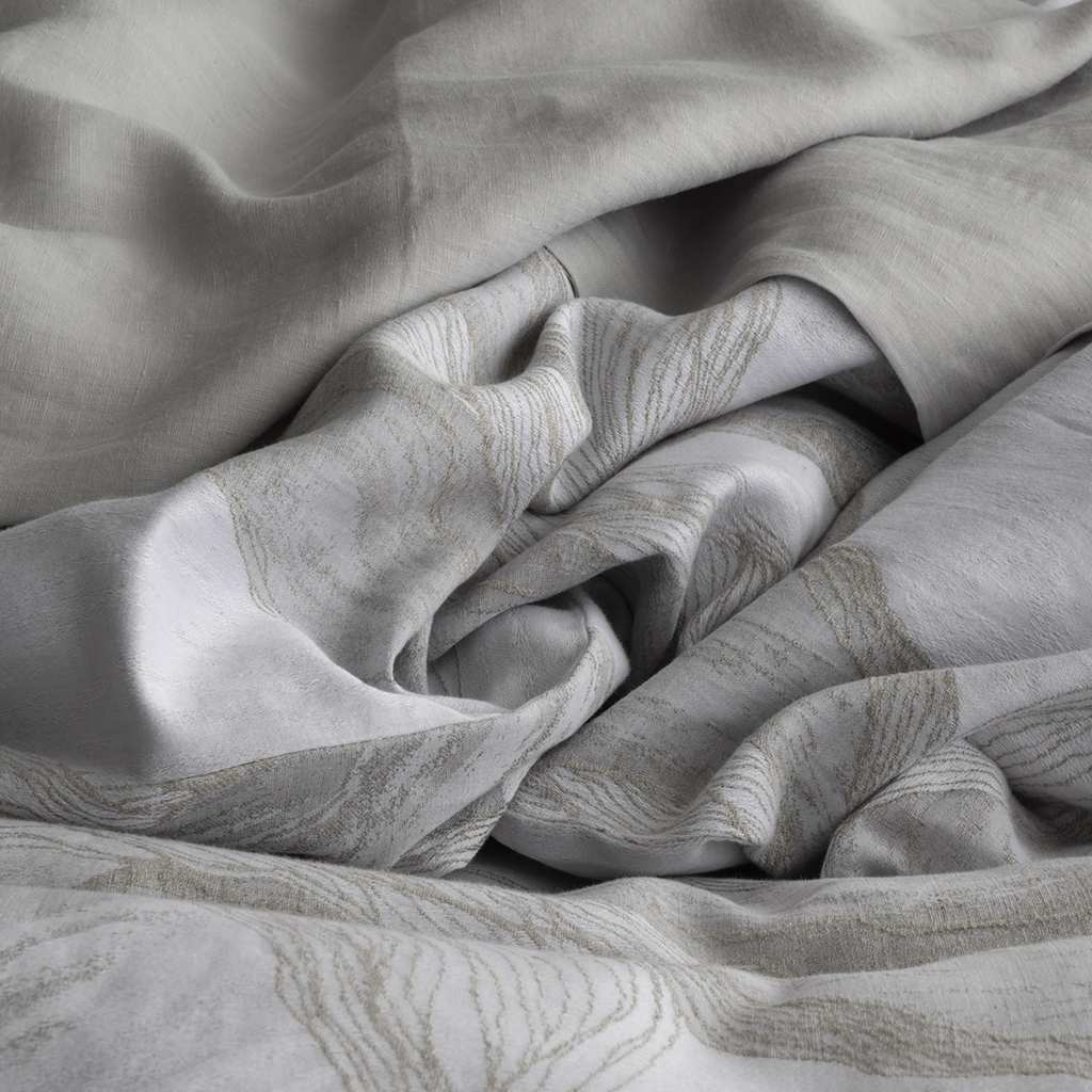A close-up of draped light gray fabric with a subtle woven wavy pattern, shown in soft folds.