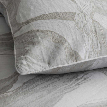 A close-up of a pillow sham with a textured, abstract botanical pattern in beige and gray on a white background, resting on matching patterned bedding.